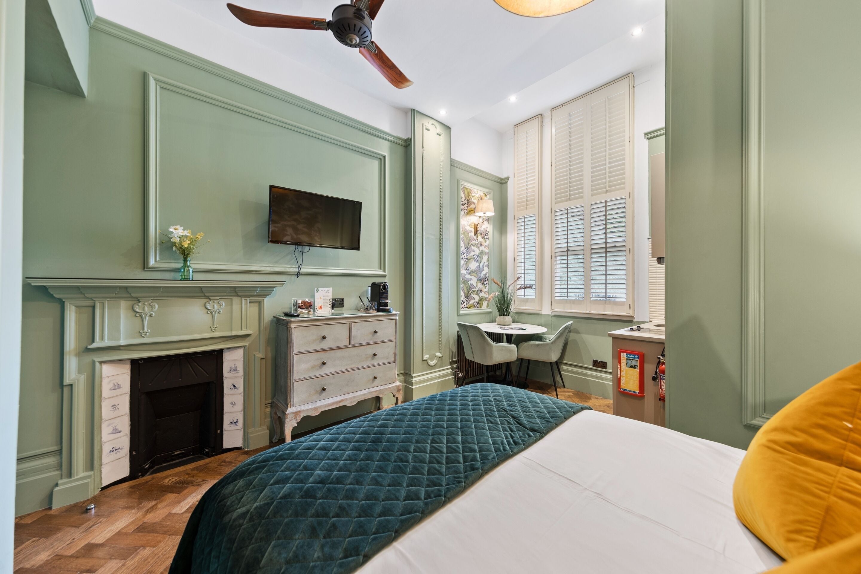 A bedroom with a bed, a desk, a fireplace, and a ceiling fan.