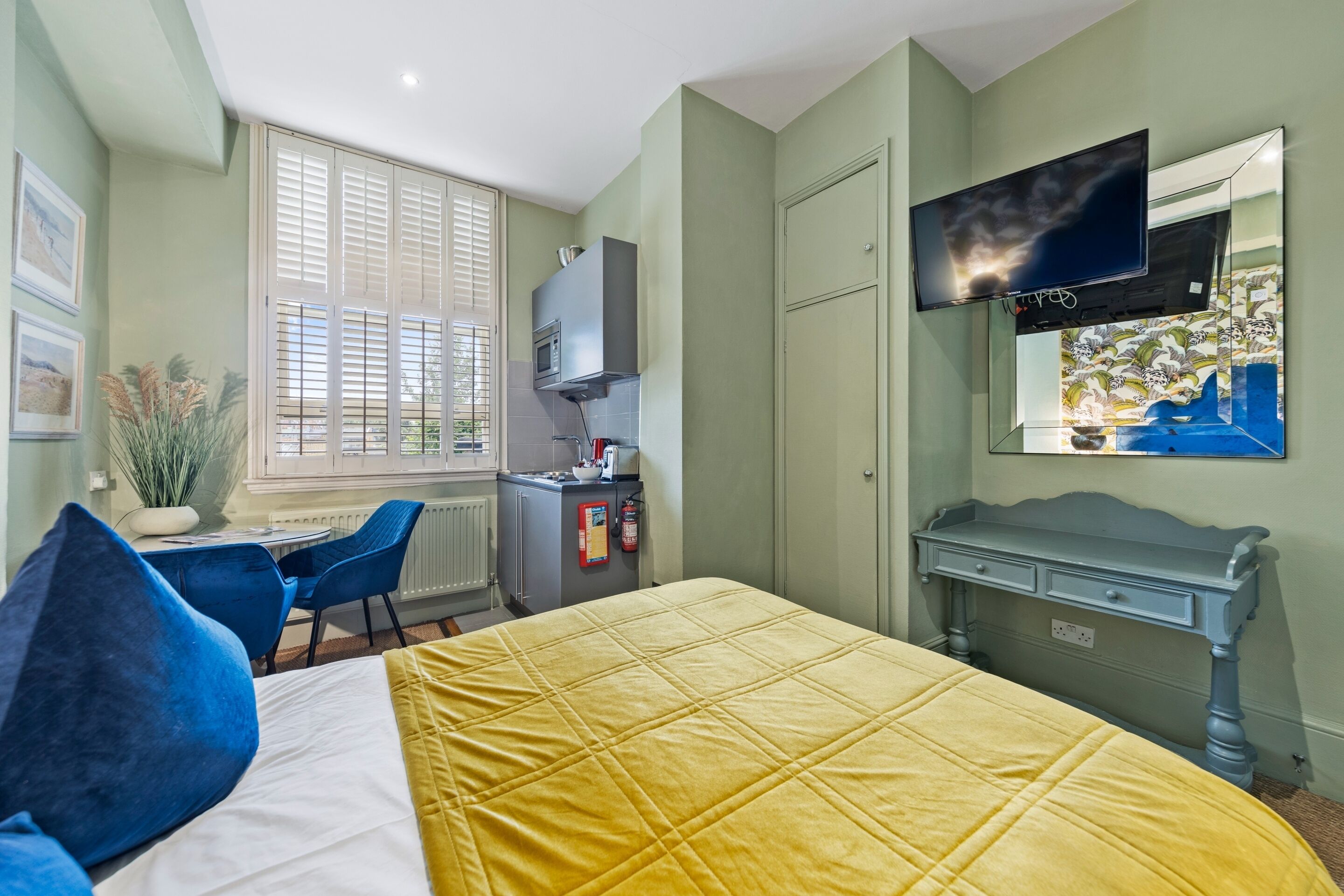Una habitación con cama, escritorio, silla, televisor y ventana con persianas.