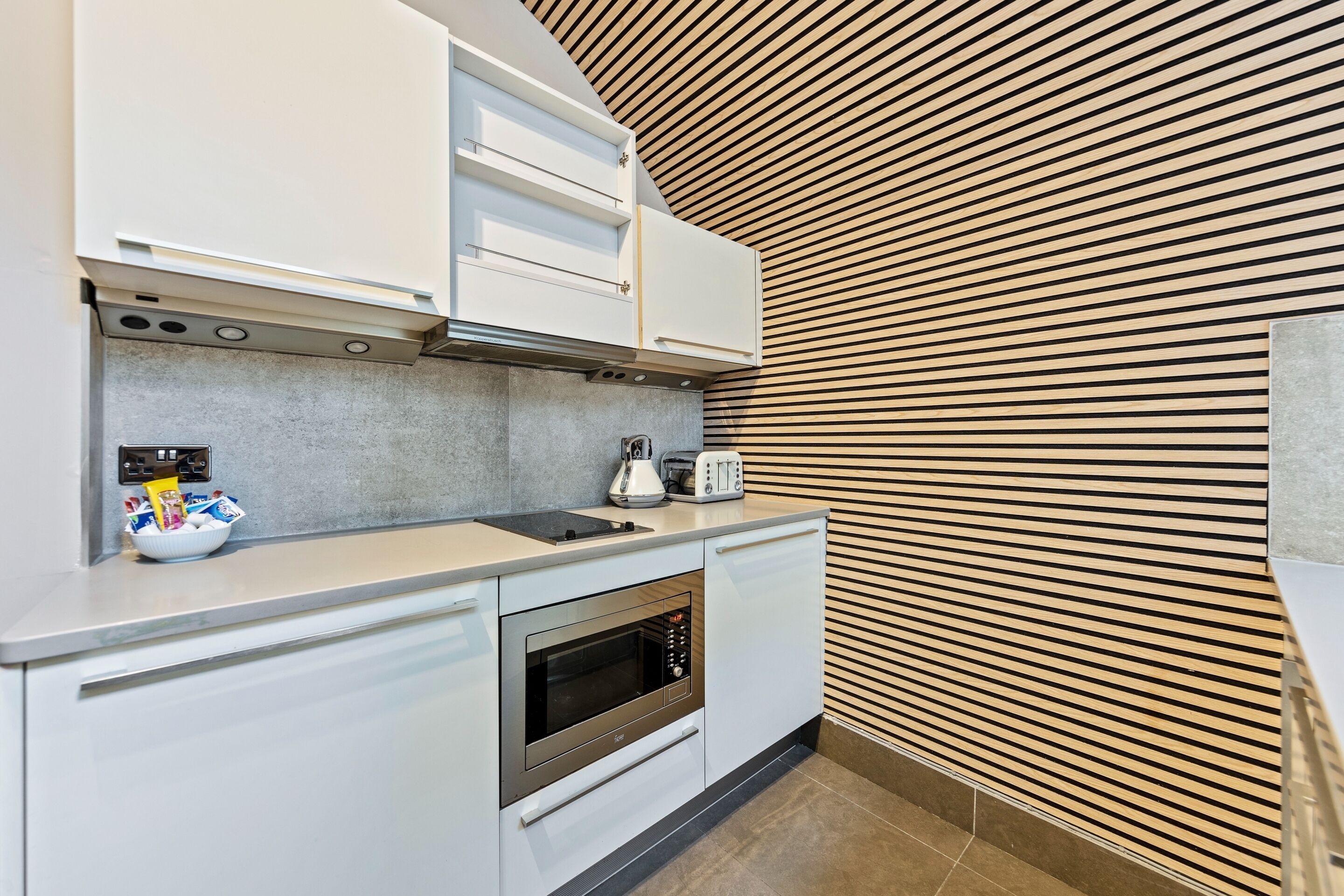 A modern kitchen with white cabinets, a built-in oven, and a wooden slatted wall.
