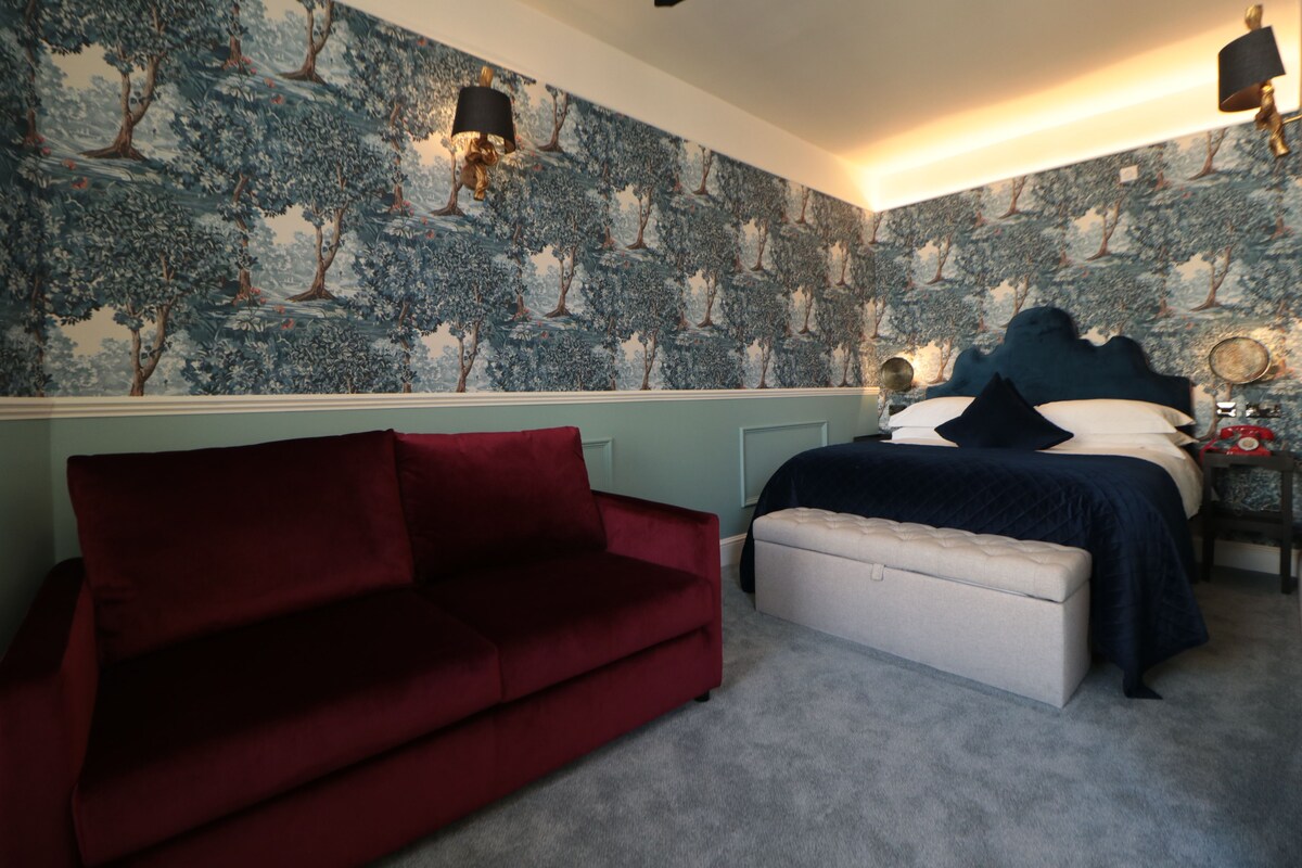 A bedroom with a bed, a red sofa, and a patterned wallpaper.