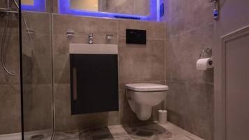A modern bathroom with a glass shower enclosure, a sink with a black cabinet, and a toilet.