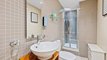 A modern bathroom with a large white sink, a toilet, and a glass-enclosed shower.