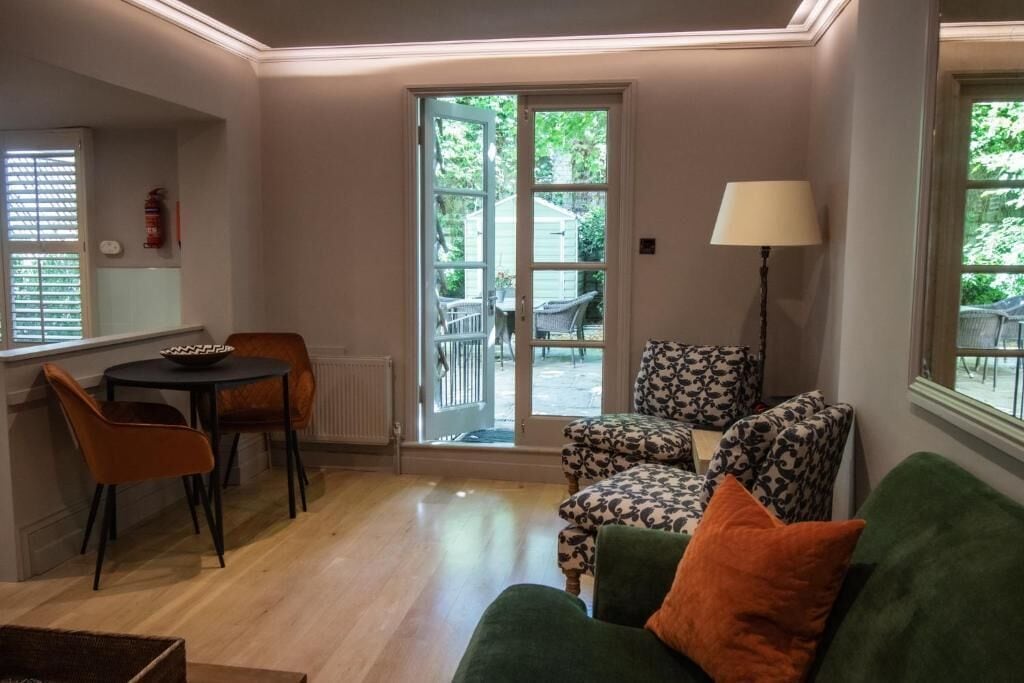 Una sala acogedora con un sofá verde, sillones estampados, una mesita y una lámpara.