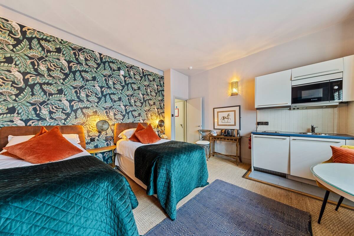 Une chambre avec deux lits, un coin cuisine et un mur décoré d’un motif.