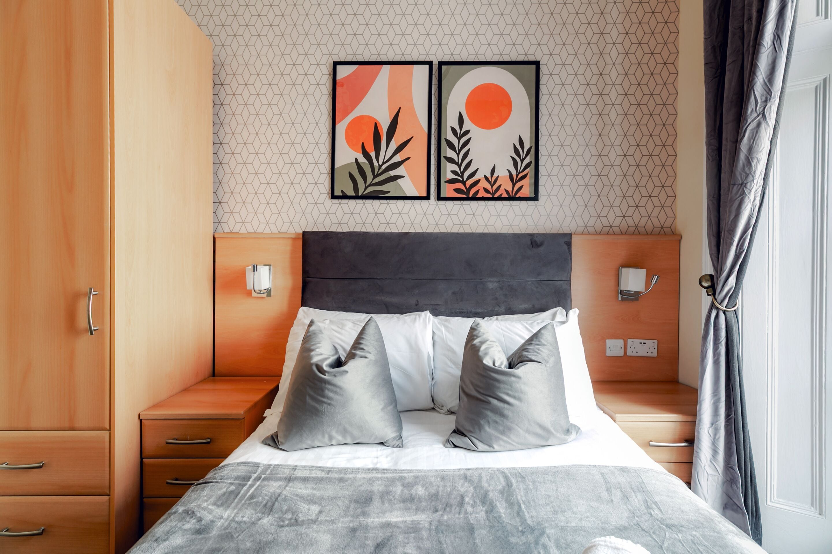 A bedroom with a bed, two bedside tables, a wardrobe, and two wall-mounted lights.