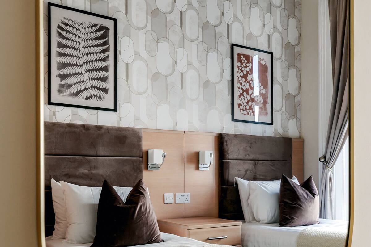 A hotel room with two beds, a large mirror, and artwork on the walls.