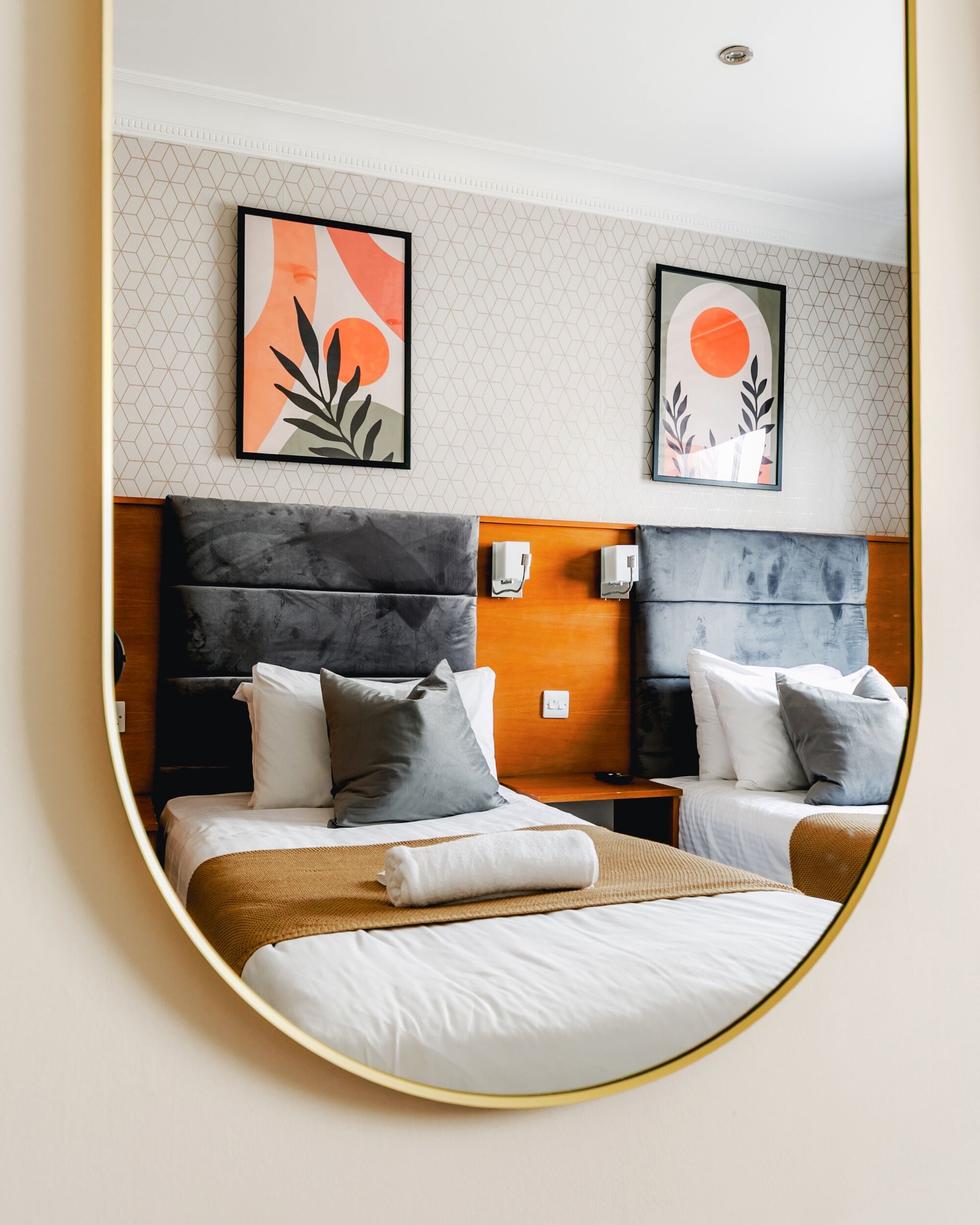 A hotel room with two beds, a large mirror, and artwork on the wall.