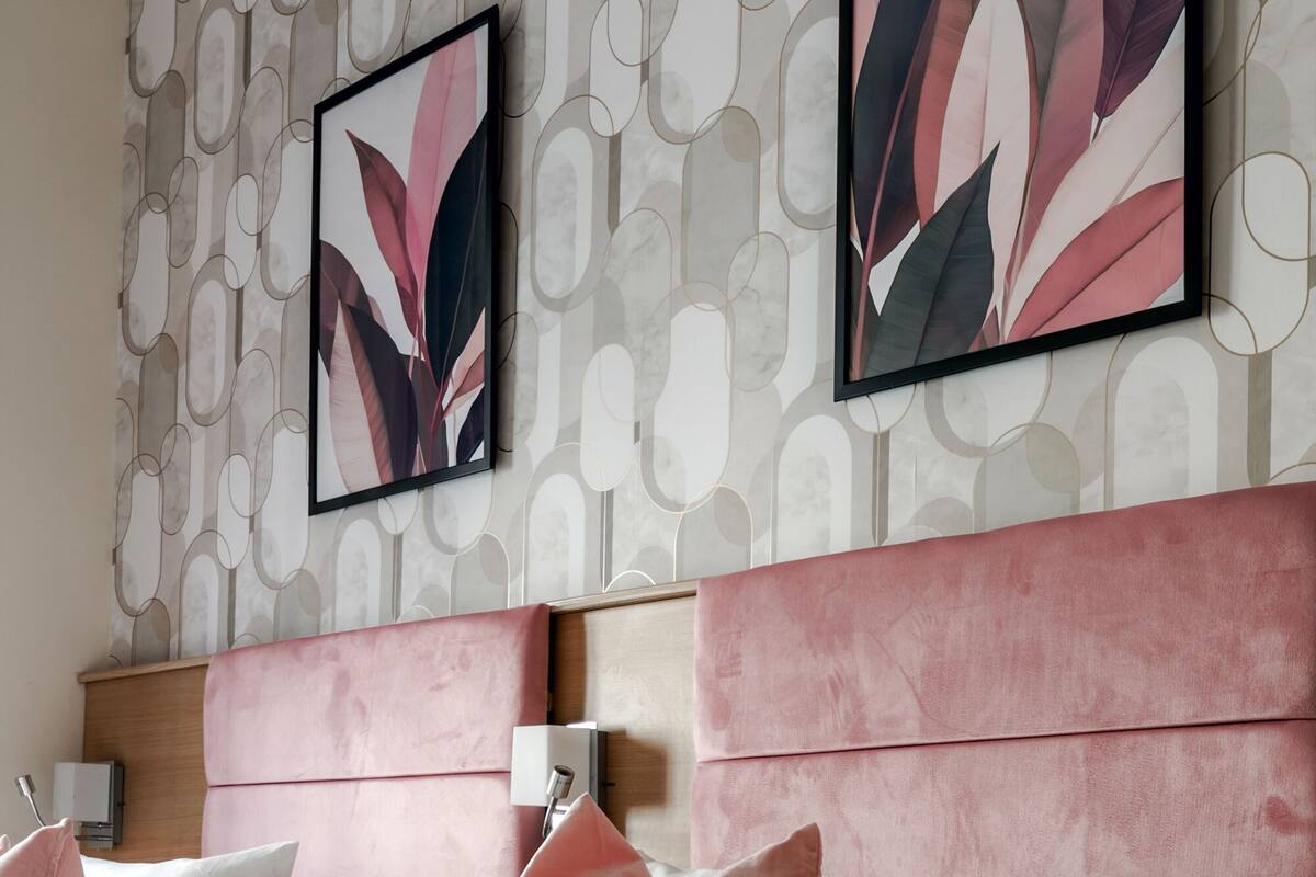 A modern hotel room with a large bed, pink and white bedding, a headboard, and abstract wall art.