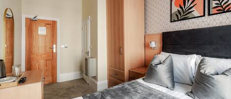 A hotel room with a bed, bedside table, wardrobe, and a wall with artwork.