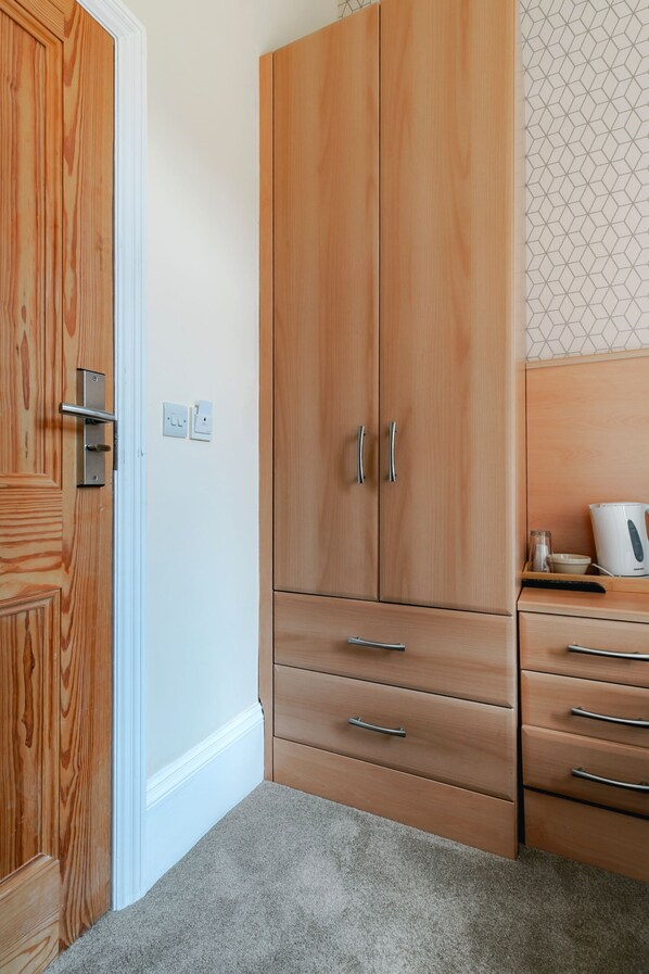 A room with wooden wardrobe, a white wall, and a patterned wallpaper. - Mina Hotel by PLI (London)