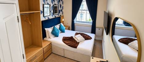 Habitación de hotel con cama, armario, escritorio con espejo y ventana con cortinas.