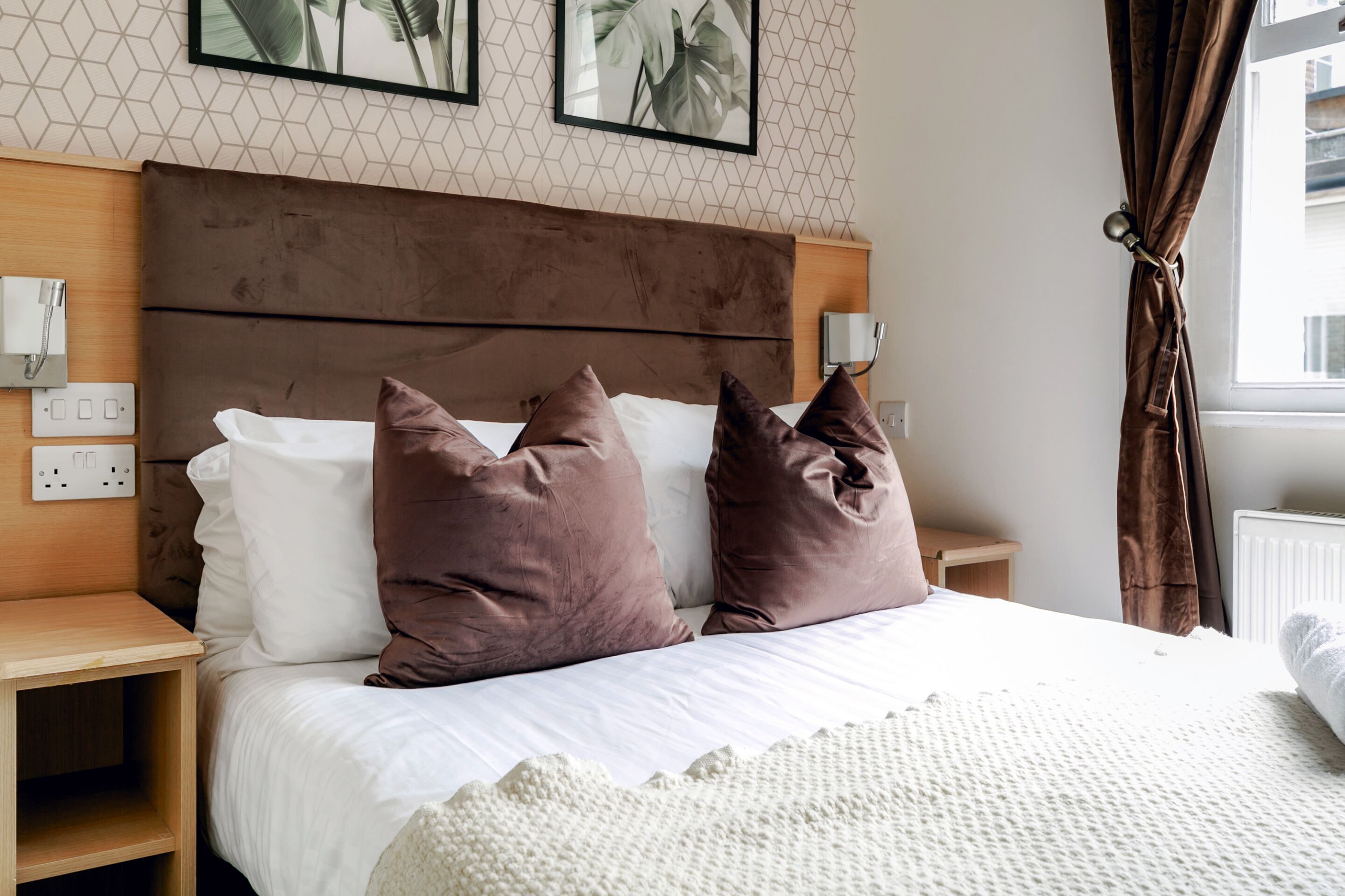 A neatly made bed with a brown headboard, two bedside tables, and a wall-mounted light fixture.