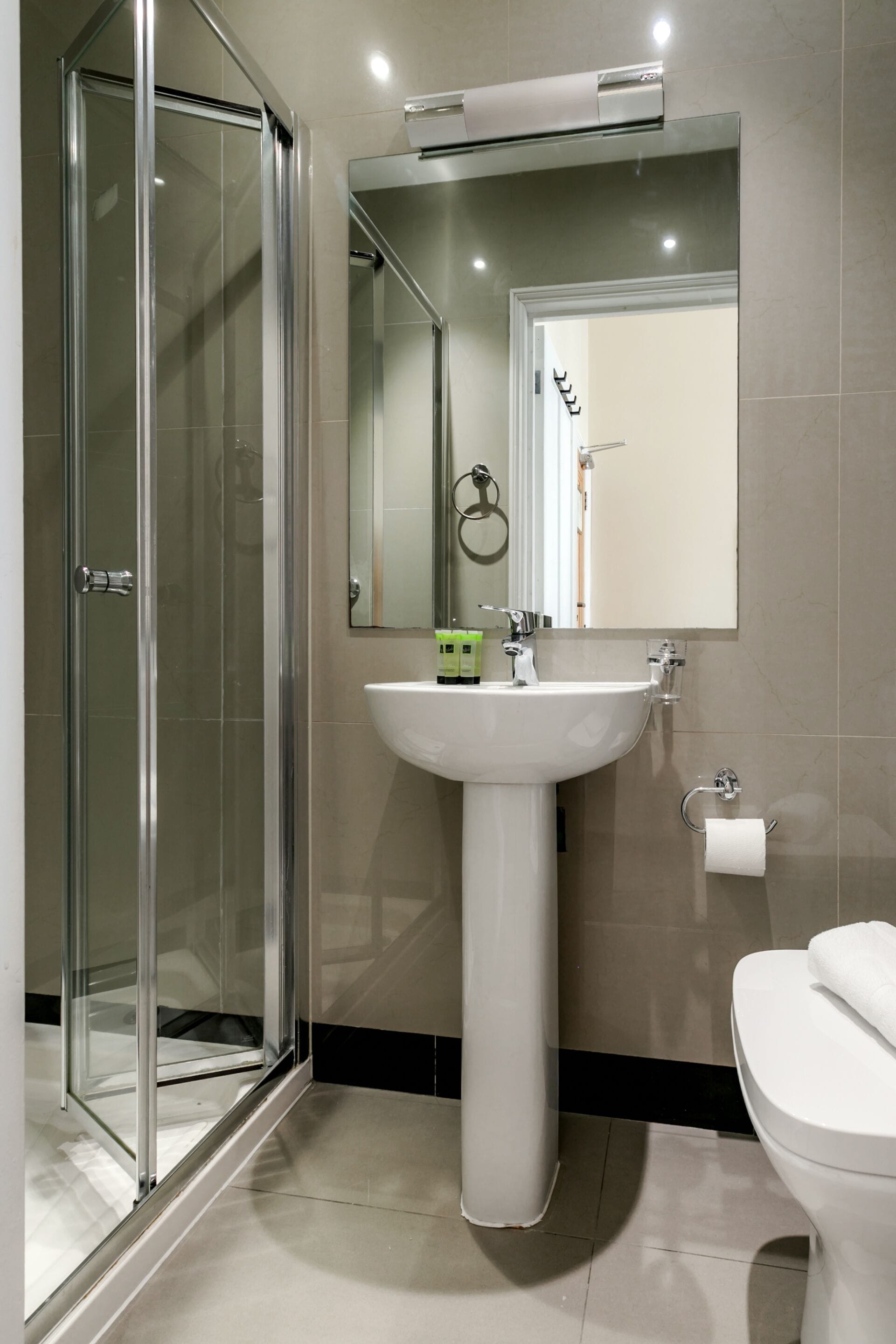 Un baño con cabina de ducha de vidrio, un lavamanos blanco, un espejo y un inodoro.