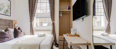 A hotel room with a bed, a desk, a TV, a wardrobe, and a window with curtains.