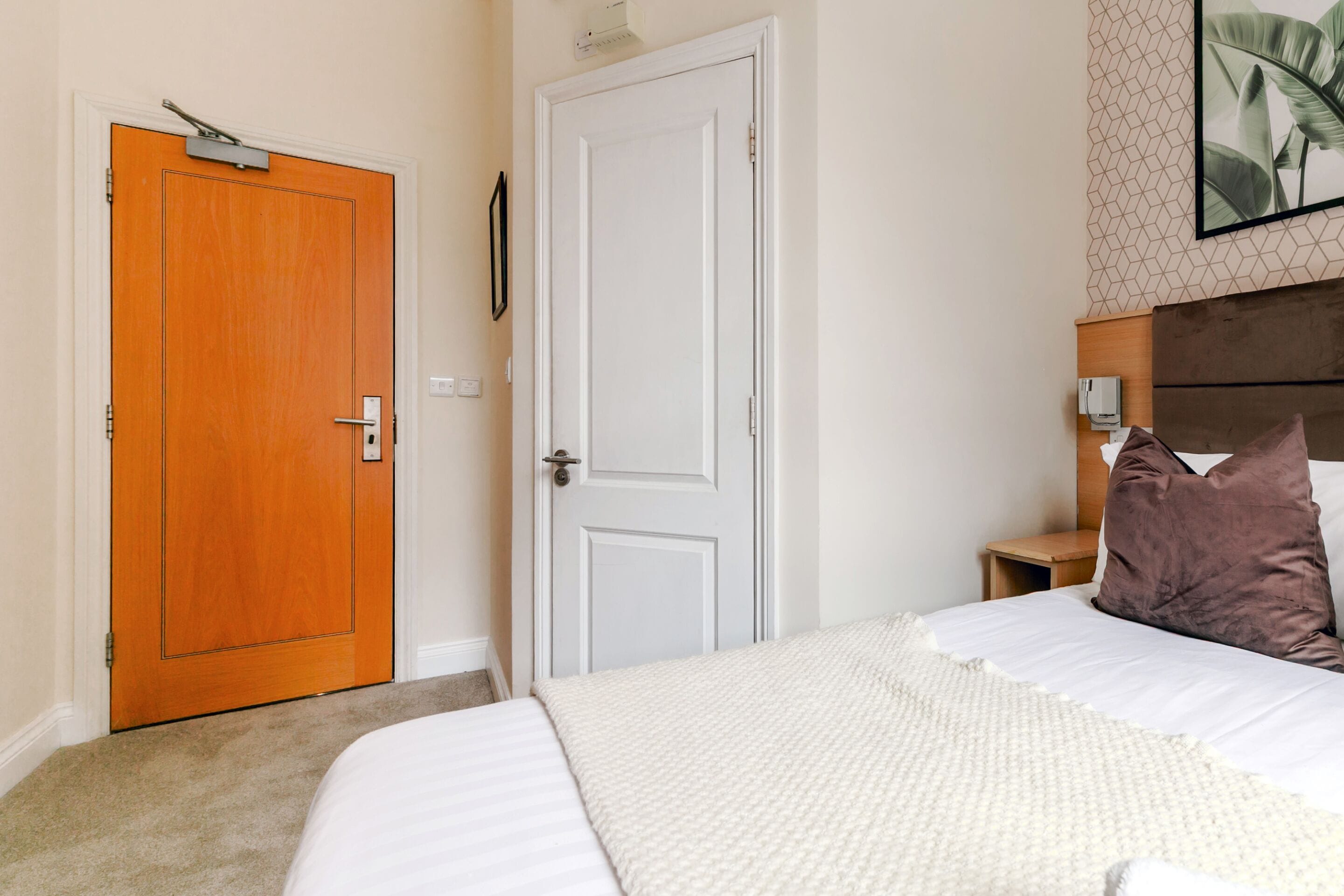 A bedroom with a bed, two doors, a nightstand, a lamp, and a framed picture on the wall.