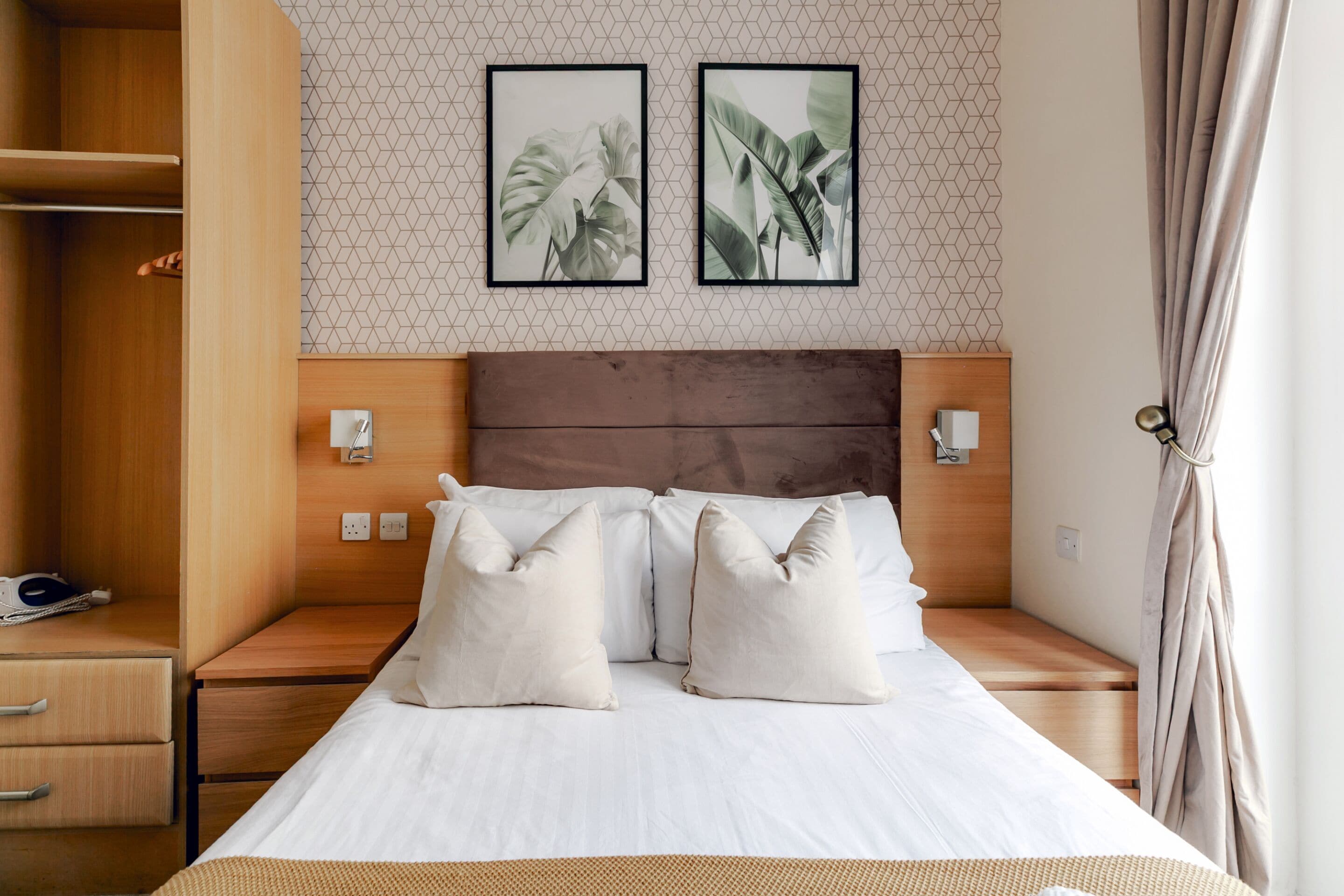 A hotel room with a wooden headboard, a bed with white bedding, two wall-mounted nightstands, and a geometric-patterned wall.