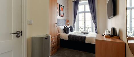A bedroom with a bed, a dresser, a radiator, a TV, and a window with curtains.