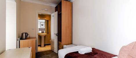 A hotel room with a bed, a wooden wardrobe, a sink, and a small table with a kettle.