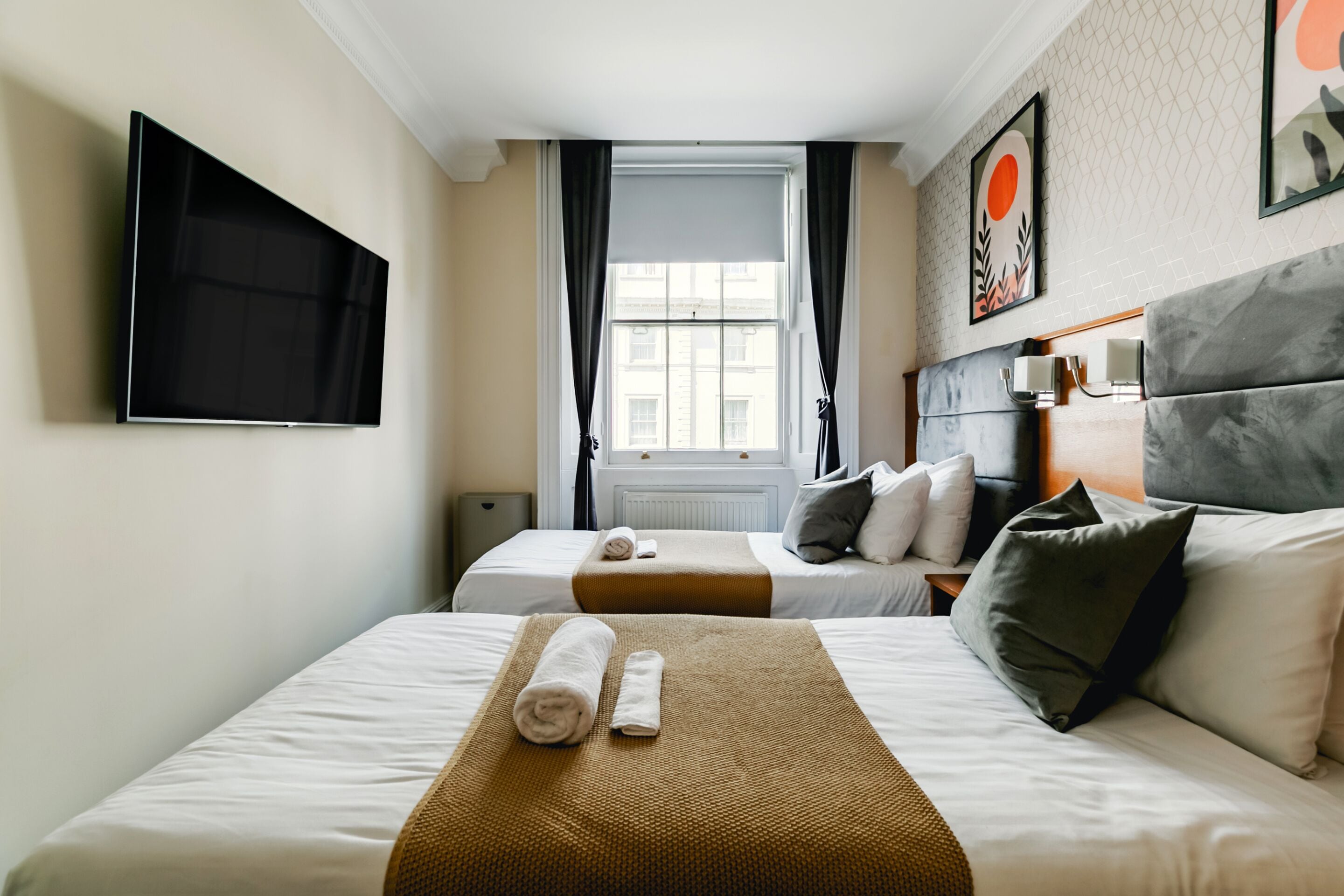 A hotel room with two beds, a TV, a window with curtains, and artwork on the wall.