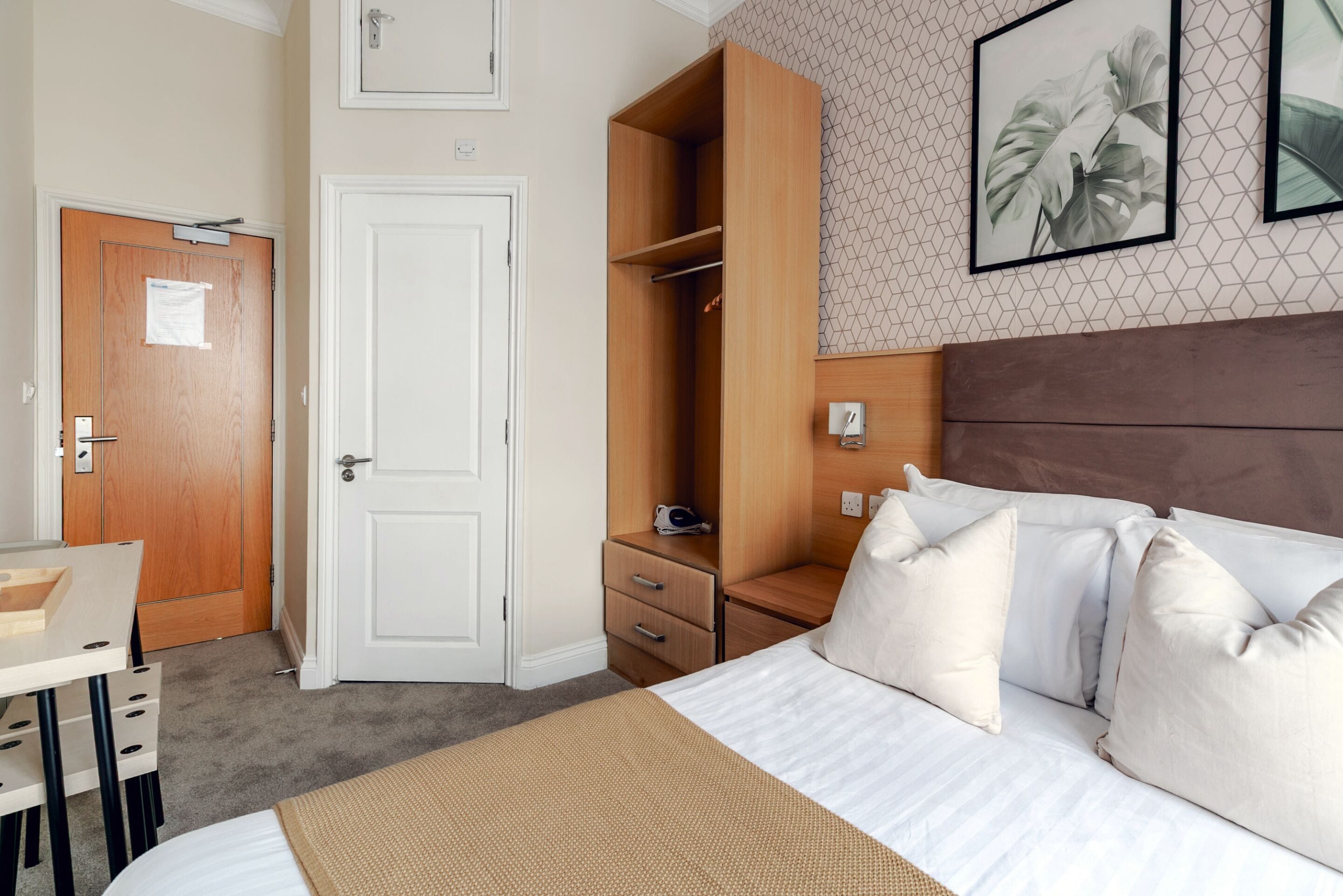 A hotel room with a bed, a desk, a wardrobe, and a door.