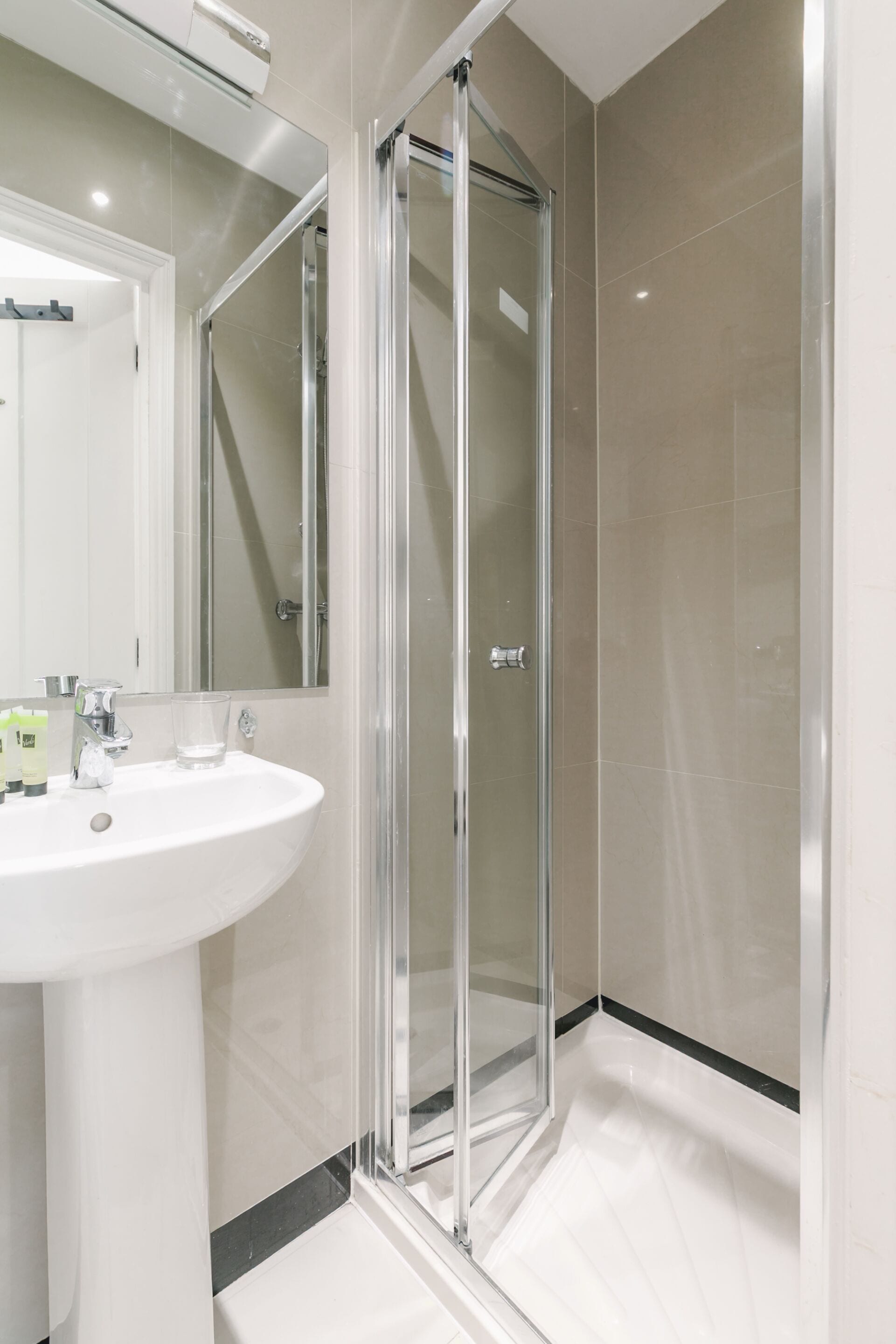 A modern bathroom with a glass shower enclosure, a white sink, and a large mirror.