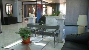 A modern lobby with a reception desk, a glass coffee table with a potted plant, and a black leather couch. - Hotel Faranda Express Las Lomas (Oviedo)