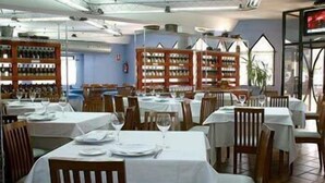 A restaurant with multiple tables set for dining, wooden chairs, and shelves with bottles in the background. - Hotel Faranda Express Las Lomas (Oviedo)