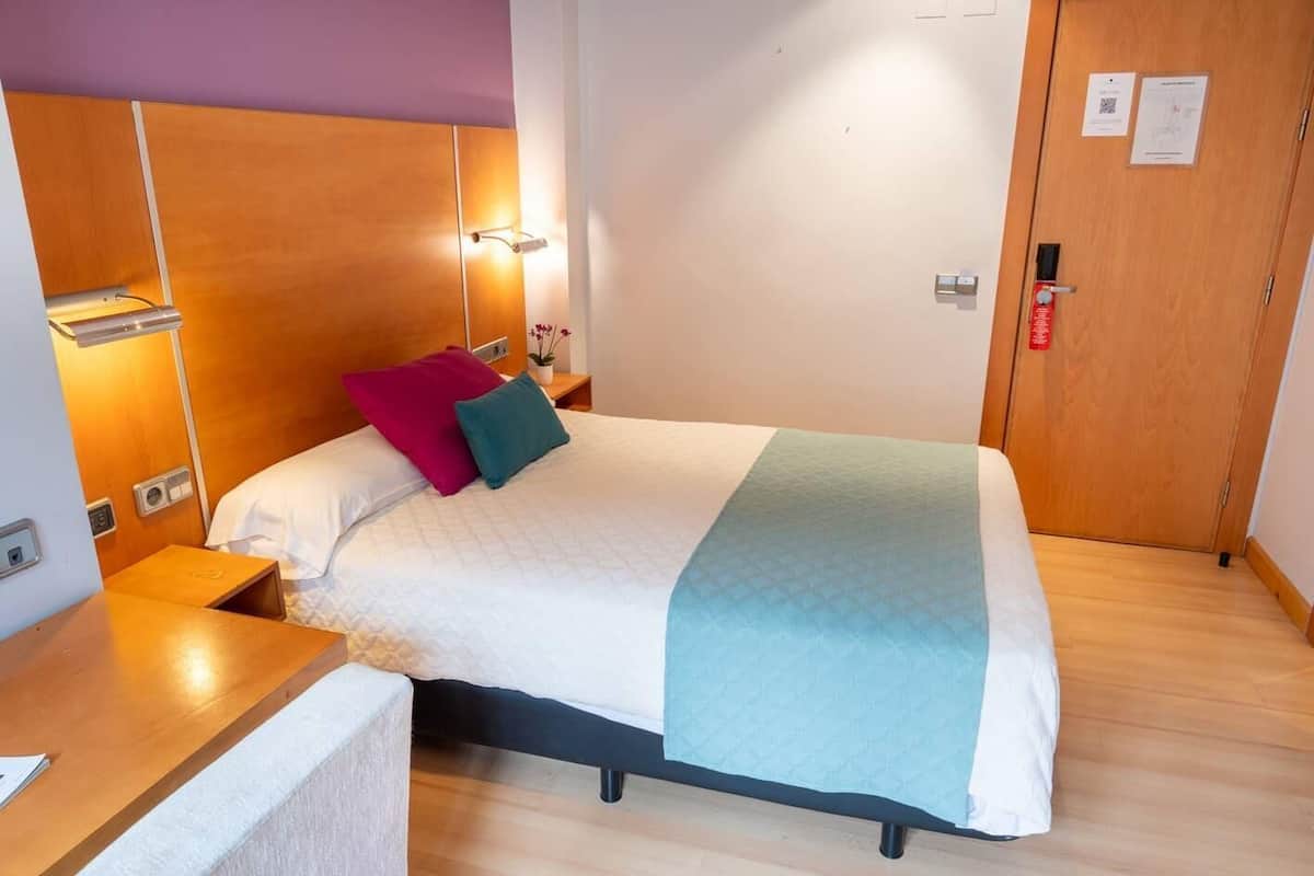 Een net opgemaakt bed met een sprei, kussens en een deken in een kamer met houten wanden en een deur.