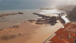 A coastal view with a pier, beach, and buildings with red roofs.
