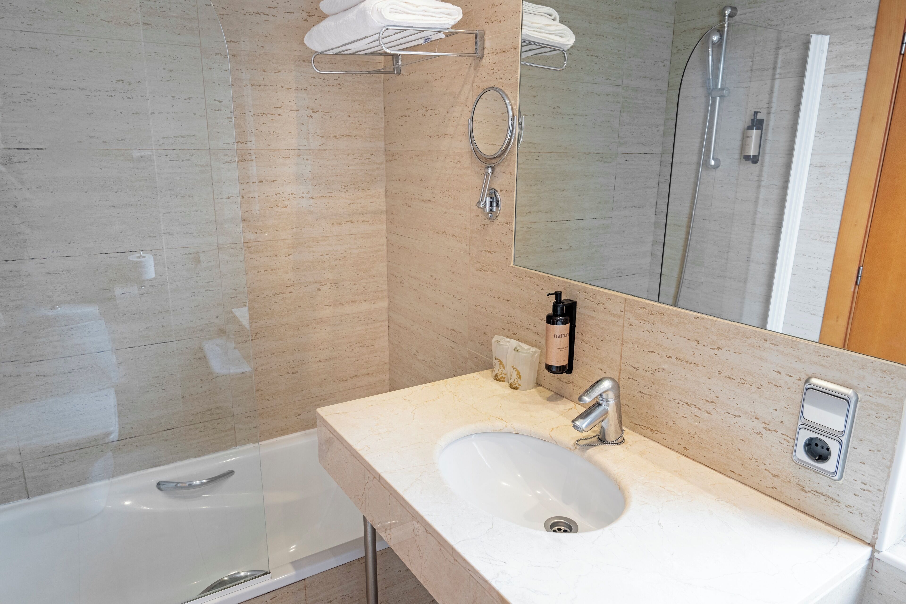 Un baño moderno con un lavamanos blanco, un espejo, un perchero para toallas y una ducha.