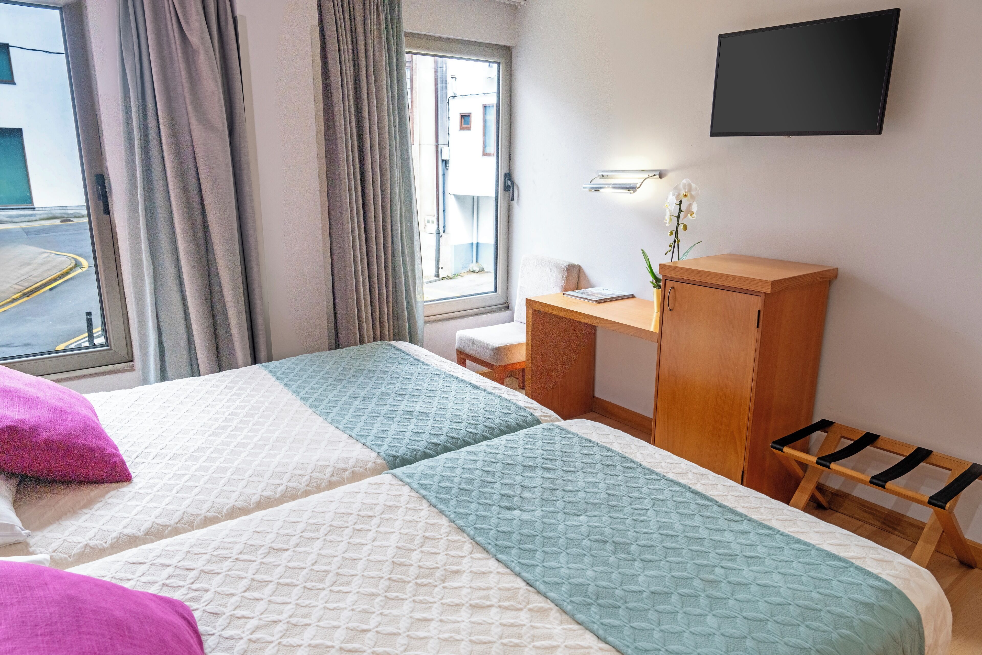 A hotel room with two beds, a desk, a TV, and a window with curtains.