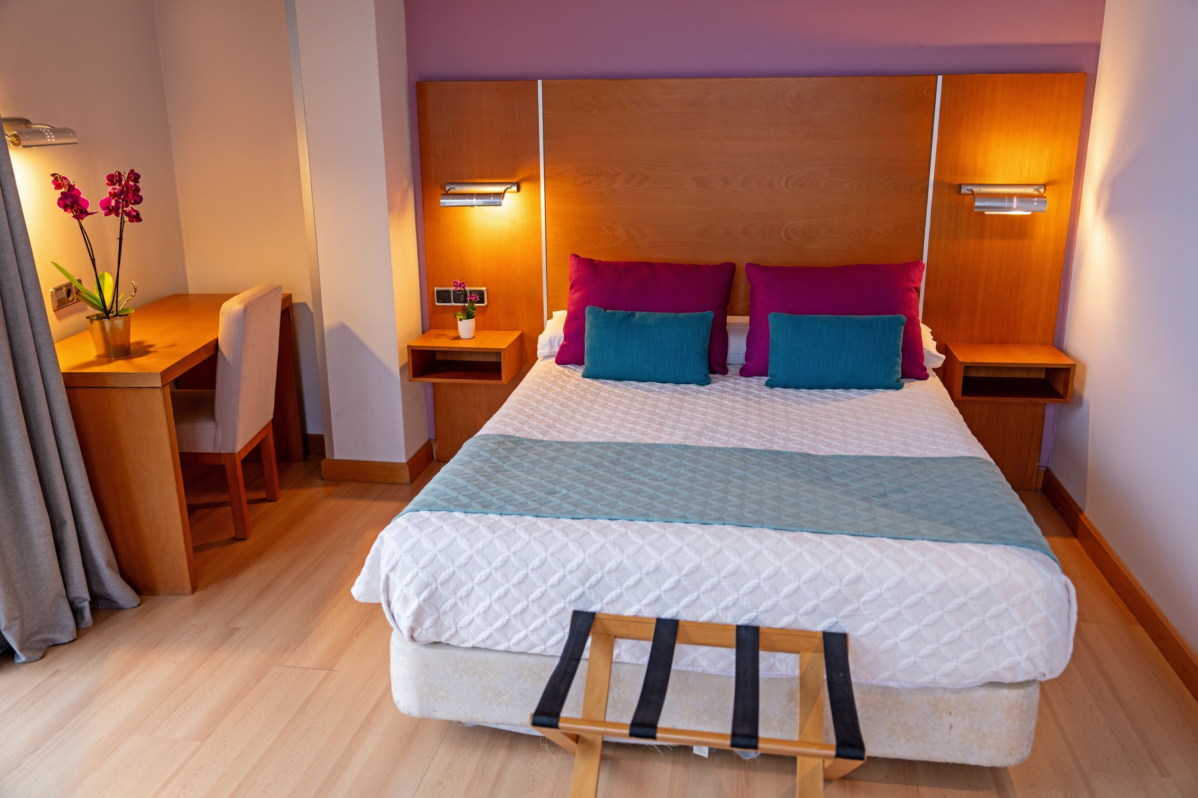 A neatly arranged bedroom with a bed, bedside tables, a desk, and a chair.