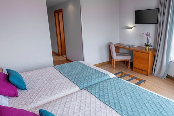 Une chambre d’hôtel avec deux lits, un bureau, une chaise, une télévision et une fenêtre avec des rideaux.
