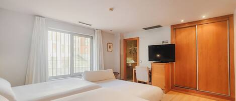 A hotel room with two beds, a TV, a wooden wardrobe, and a bathroom visible through a glass door.