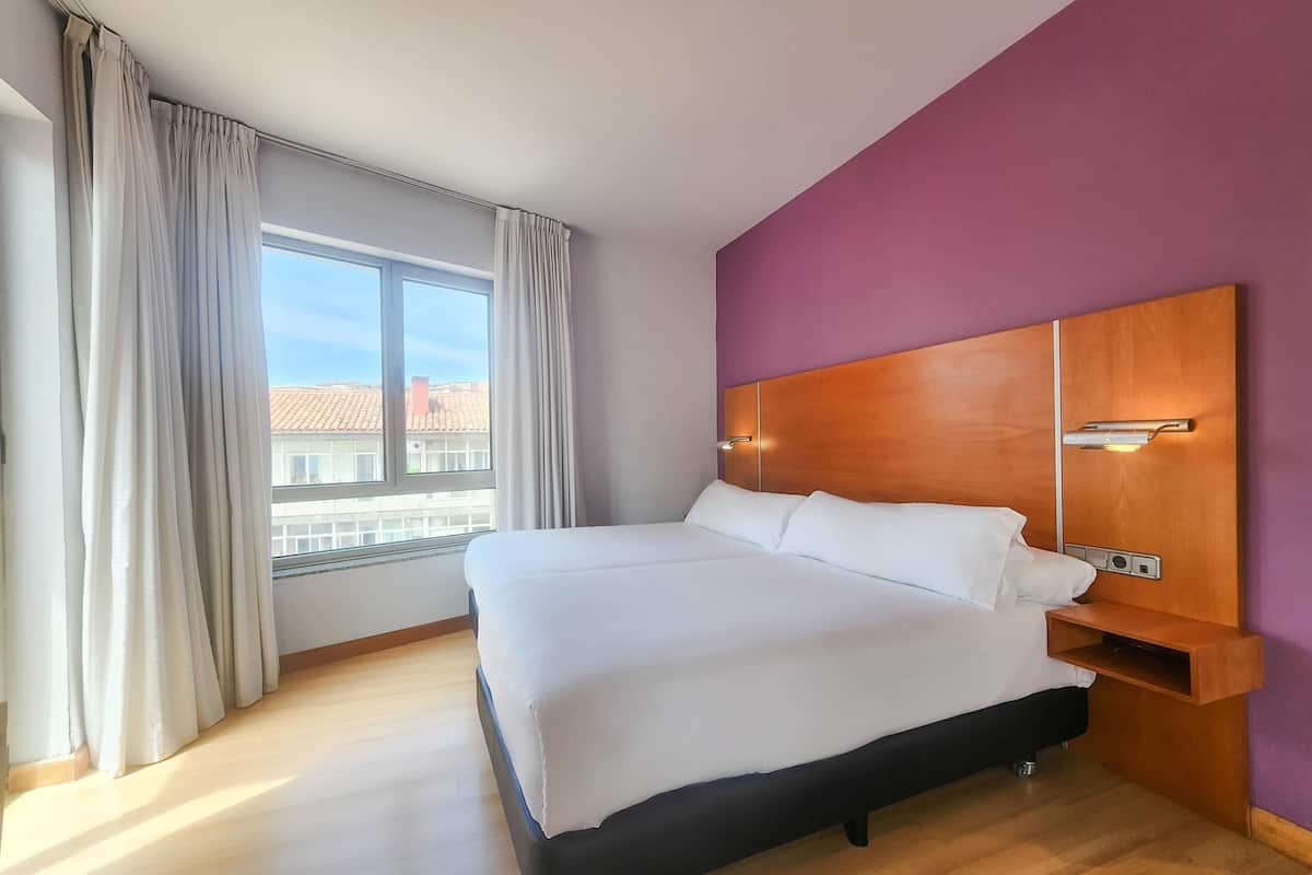 Een hotelkamer met een bed, een nachtkastje, een raam met gordijnen en een uitzicht op gebouwen.