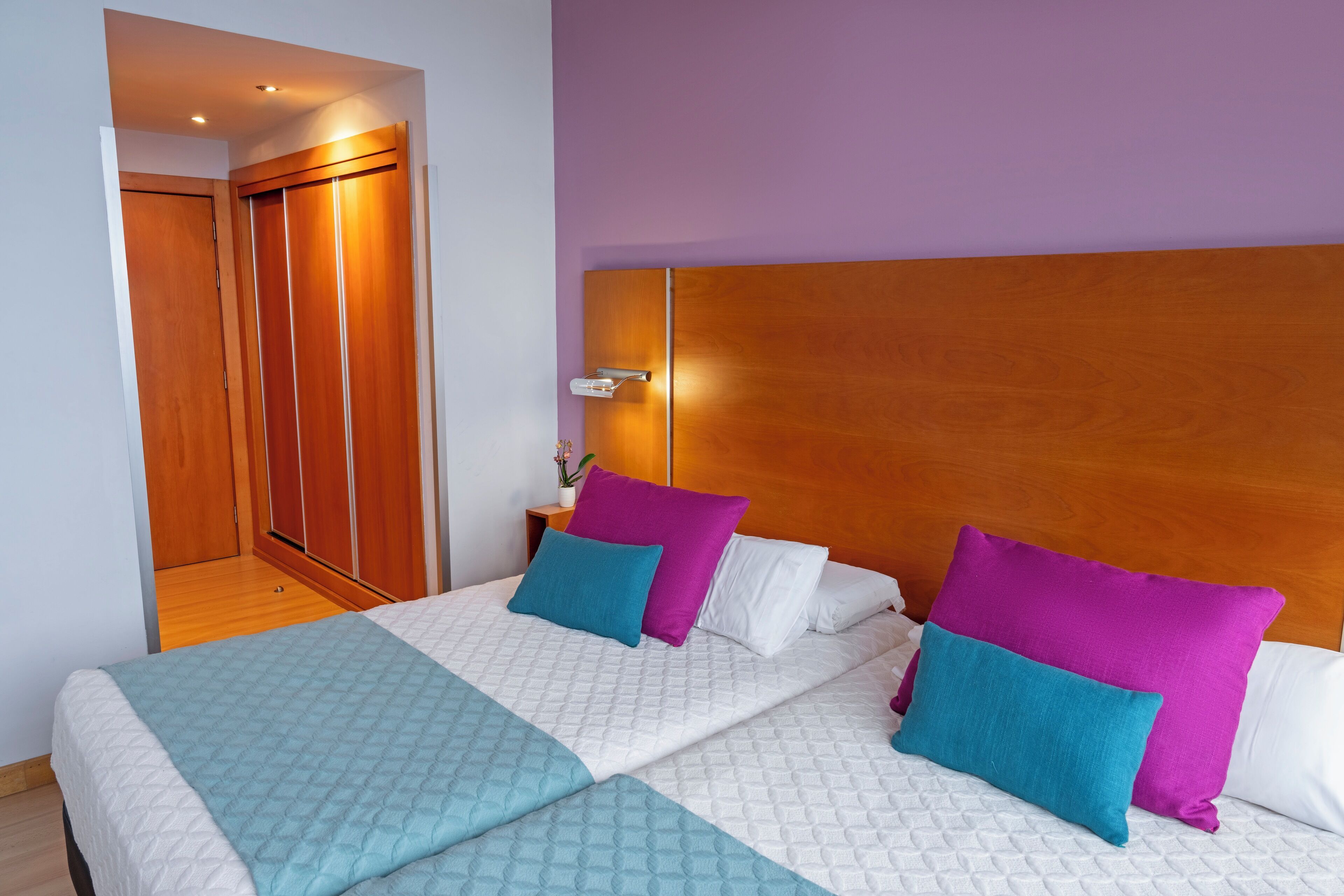 A hotel room with a large bed, a wooden headboard, and a purple wall.