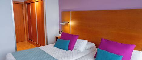 A hotel room with a large bed, a wooden headboard, and a purple wall.