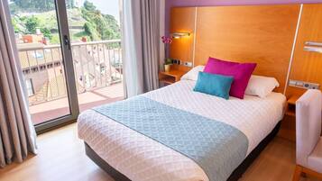Habitación de hotel con una cama grande, una mesita de noche, una lámpara y vistas a un balcón con barandilla.