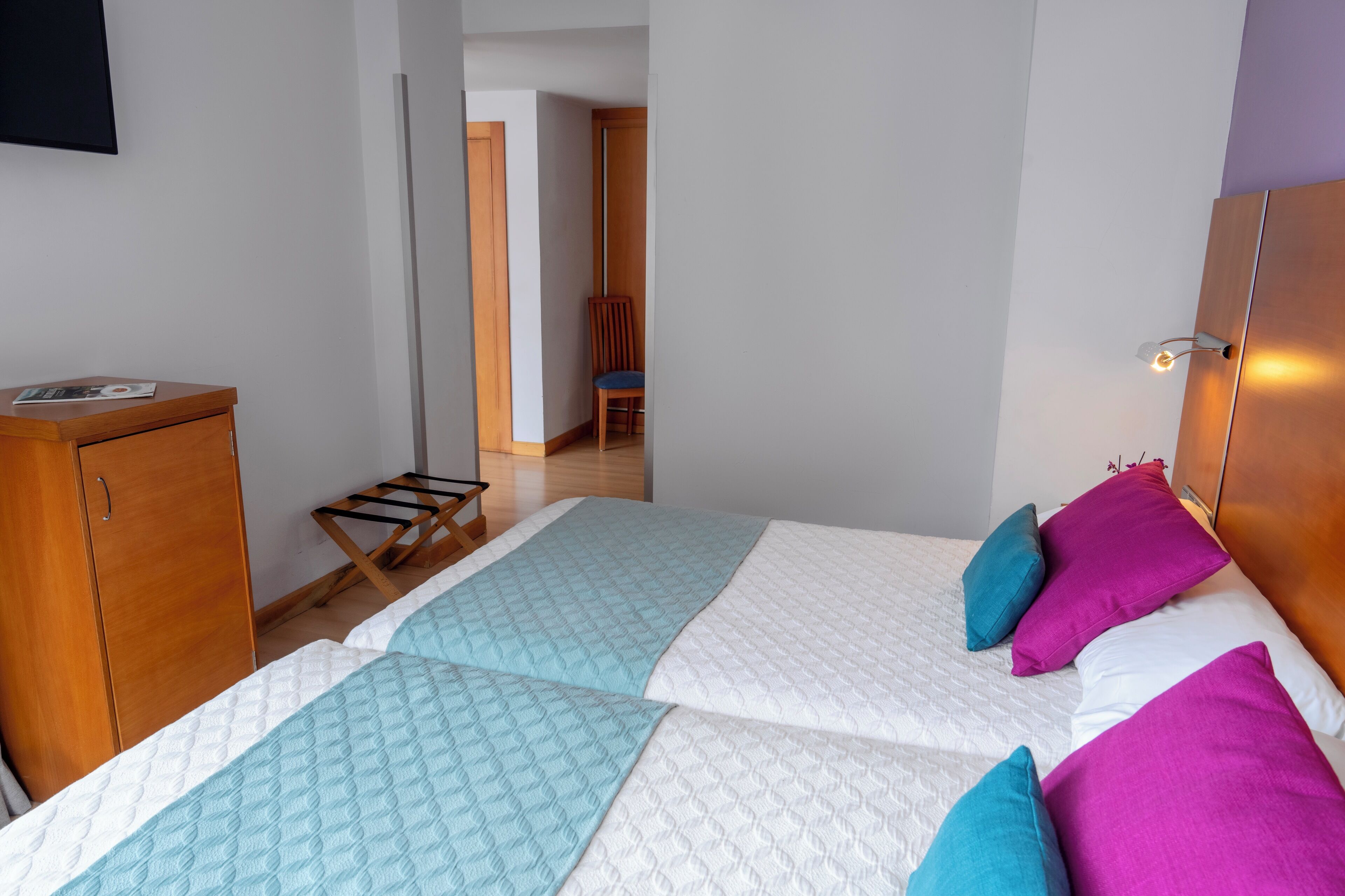 Ein Schlafzimmer mit zwei Betten, einem Holzschrank, einem Stuhl und einem kleinen Tisch.