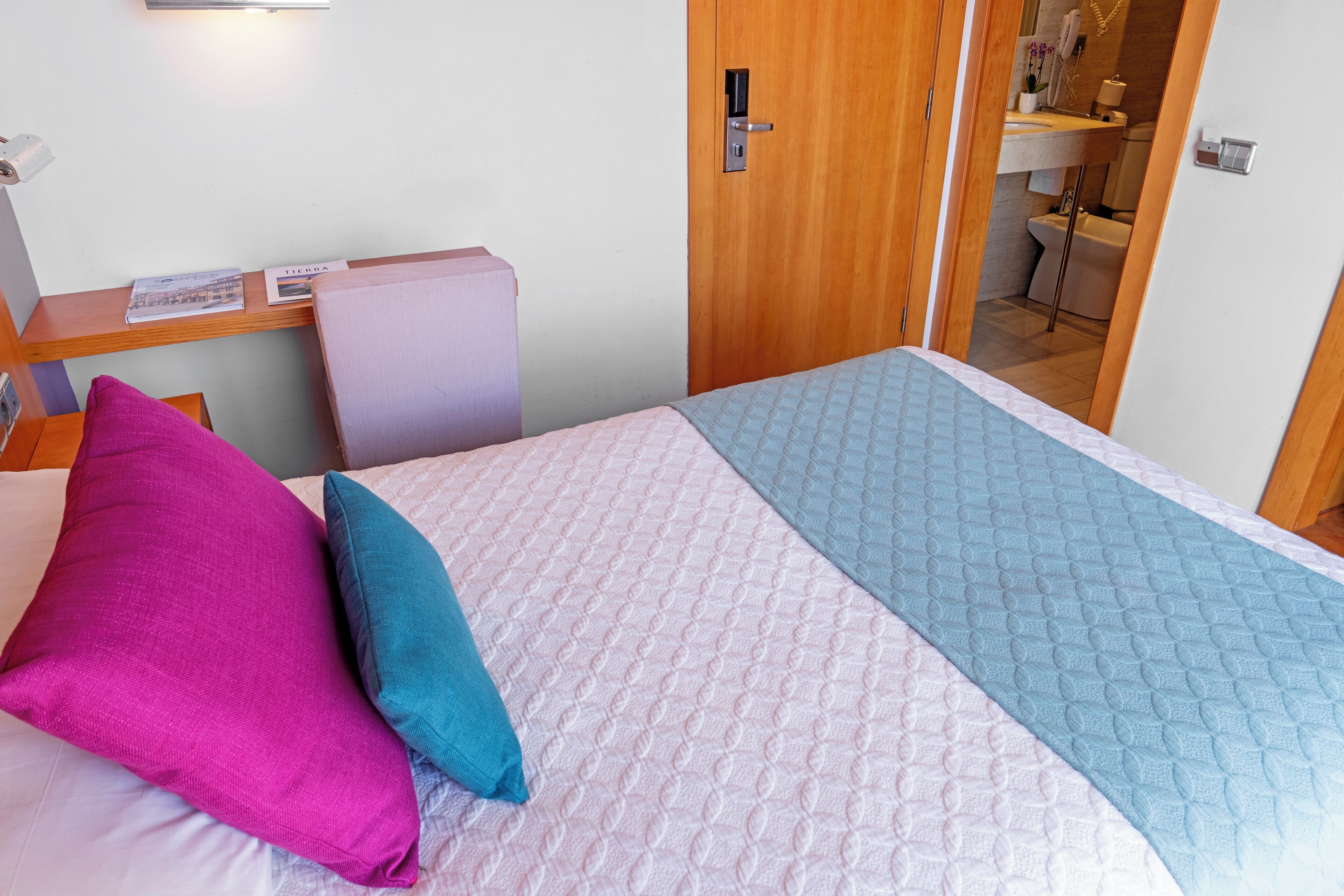 Ett hotellrum med en säng, ett skrivbord och ett badrum som syns genom en öppen dörr.