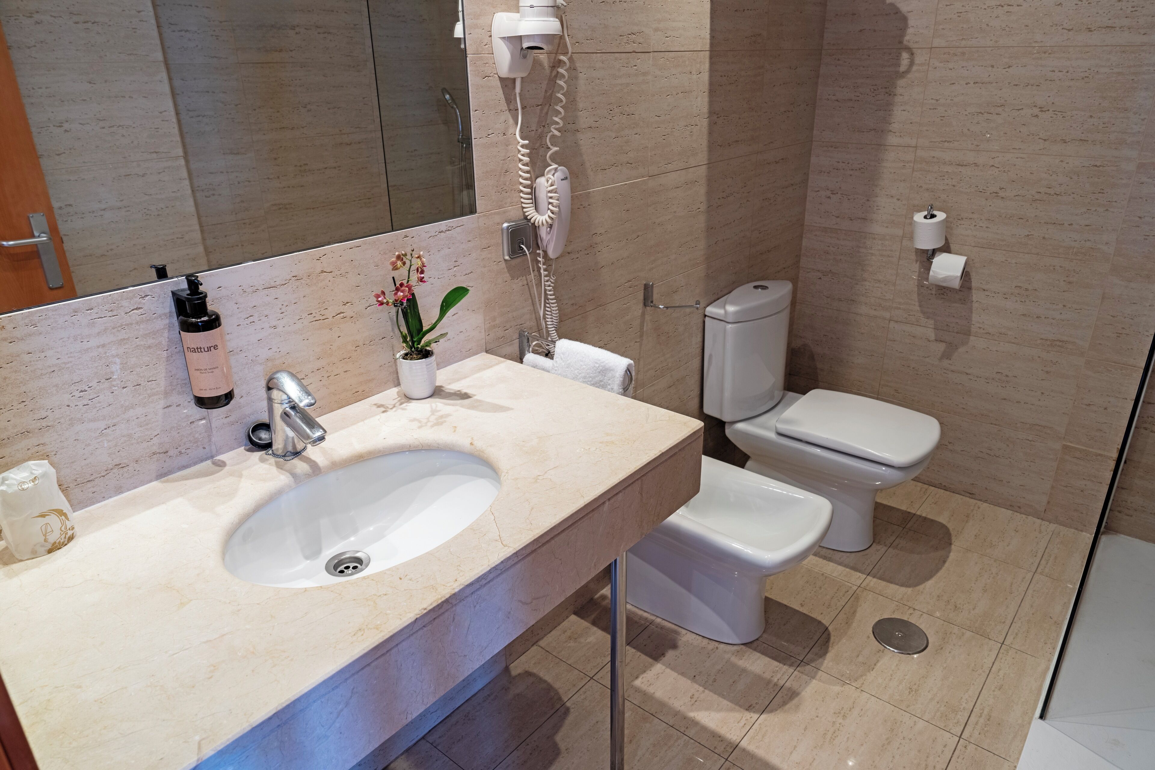 Une salle de bain équipée d’un lavabo, d’un miroir, d’un sèche-cheveux et de toilettes.