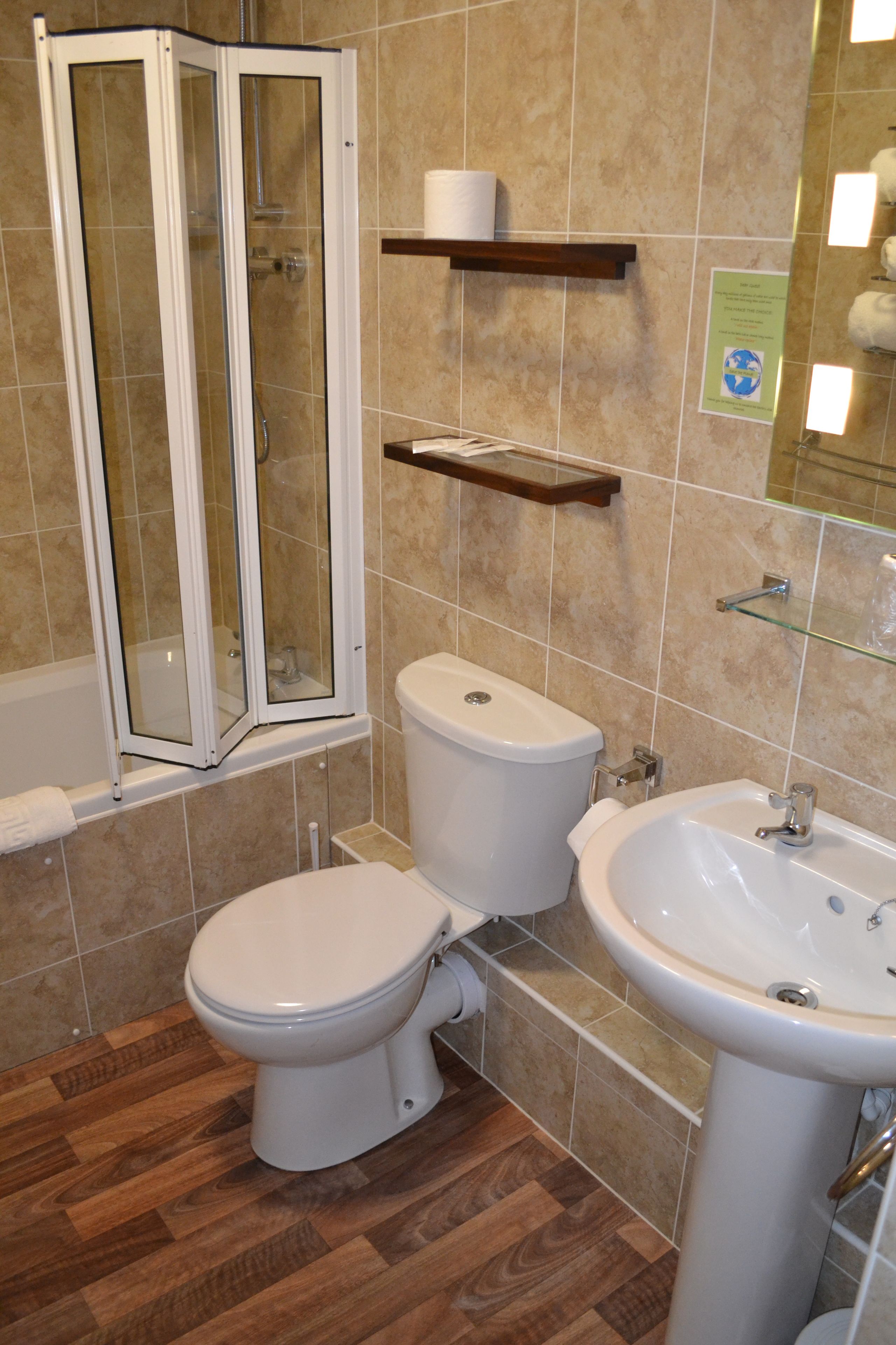 Un baño con inodoro, lavamanos, cabina de ducha y estante de madera con un rollo de papel higiénico.
