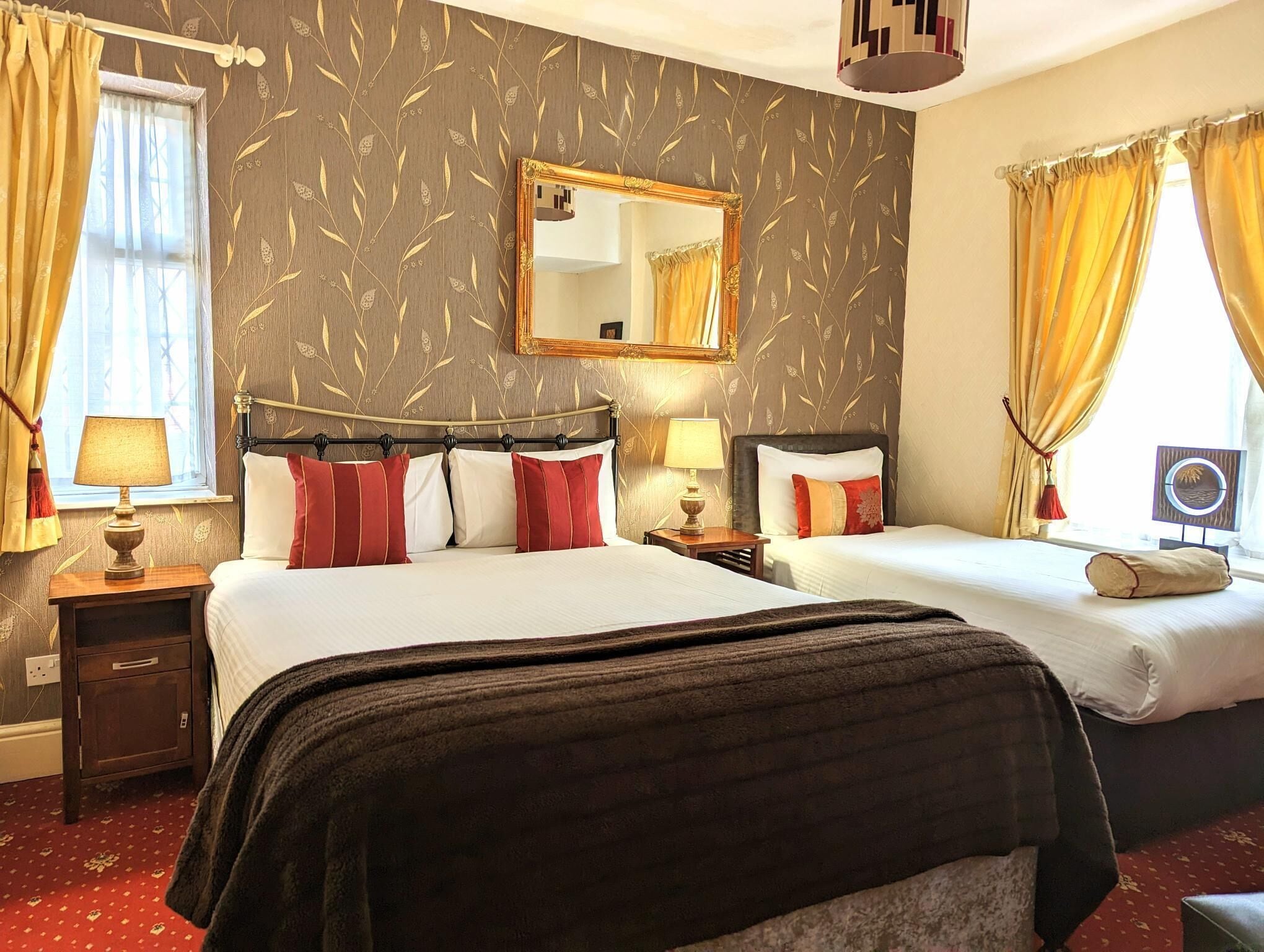 A hotel room with two beds, a large mirror, and a window with curtains.