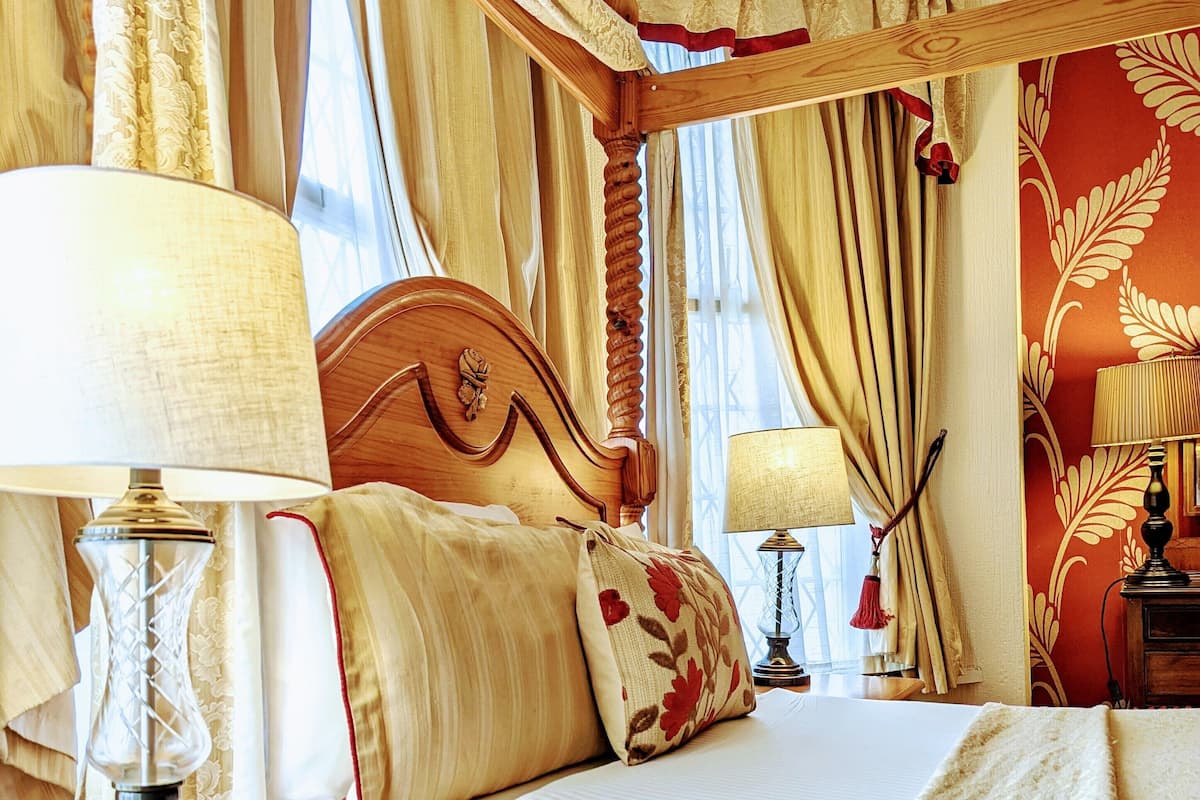 Un dormitorio tradicional con una cama de madera, dos mesitas de noche con lámparas y un ventanal con cortinas.