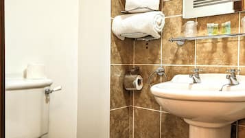 Un baño con inodoro, lavamanos, toallero y cubo de basura.