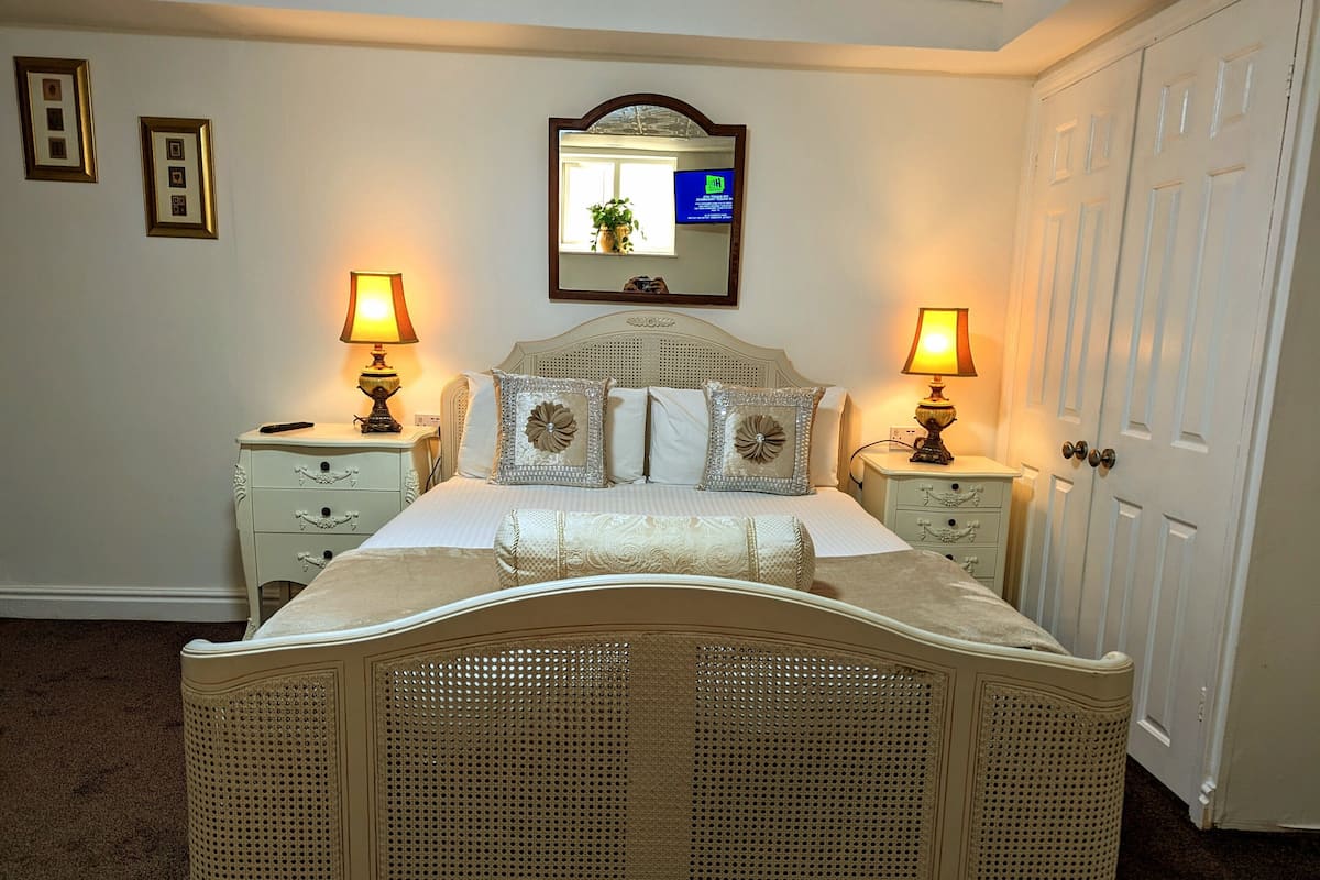 Un dormitorio de diseño clásico, con una cama con dosel, dos mesitas de noche y un espejo sobre la cama.