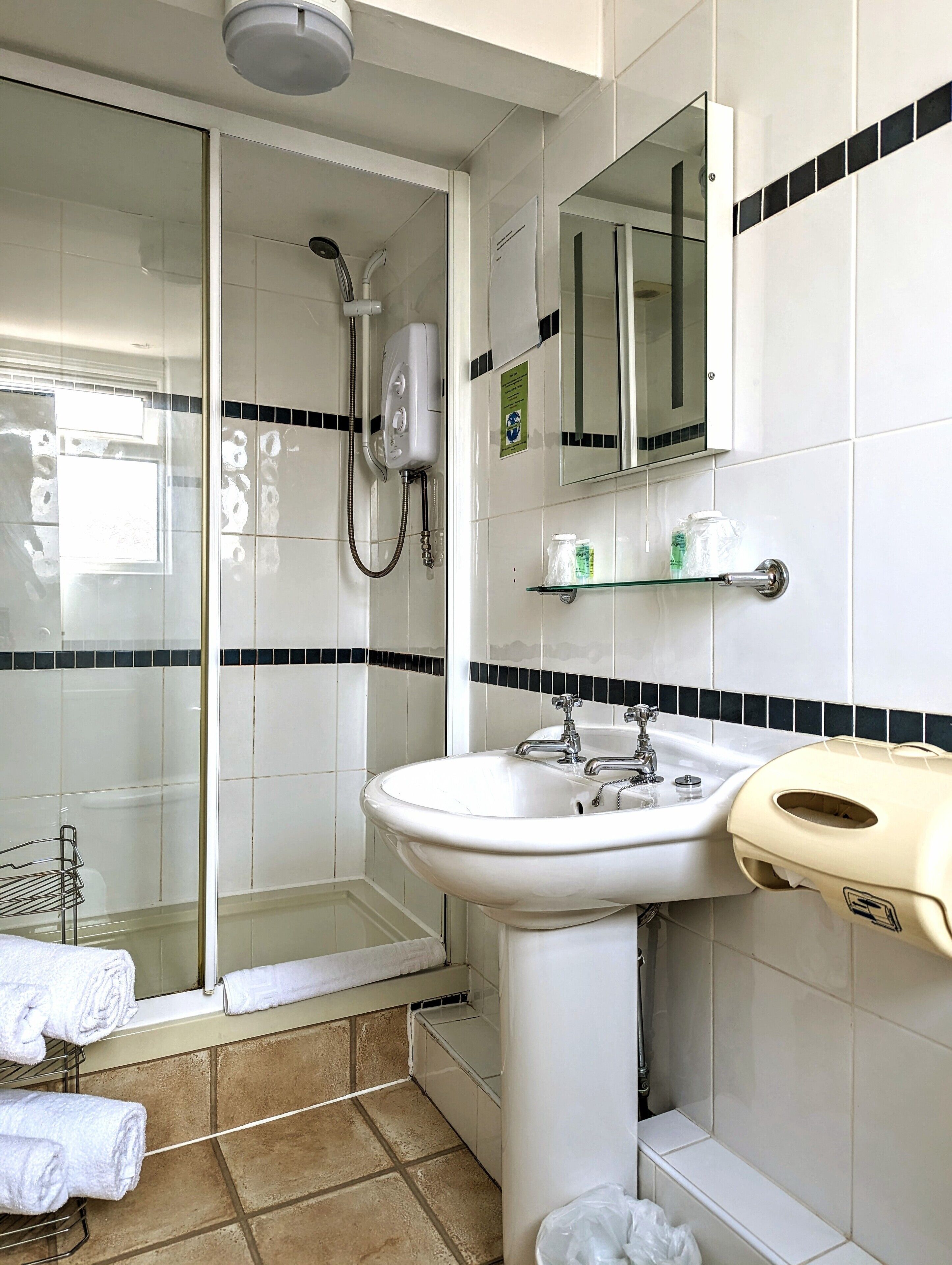 Un baño con cabina de ducha de vidrio, un lavamanos con espejo y un perchero con toallas.