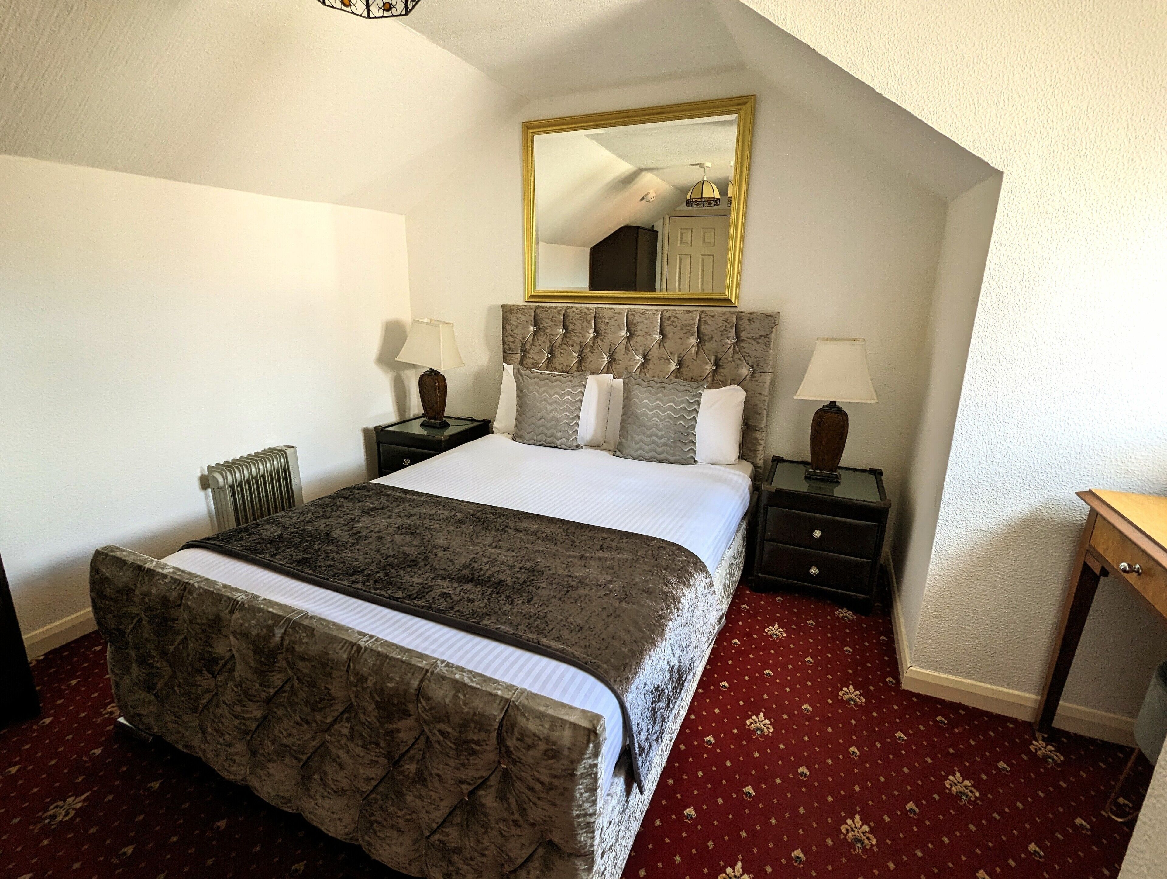 A bedroom with a large bed, two bedside tables, a nightstand, a chair, a mirror, and a red carpet.