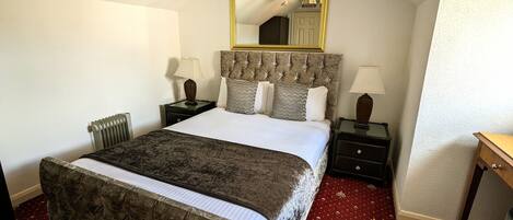 A bedroom with a large bed, two bedside tables, a nightstand, a chair, a mirror, and a red carpet.