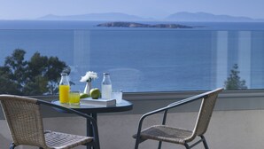 A balcony with a table set for two, overlooking a body of water and distant land. - Amarilia Hotel (Vari-Voula-Vouliagmeni)